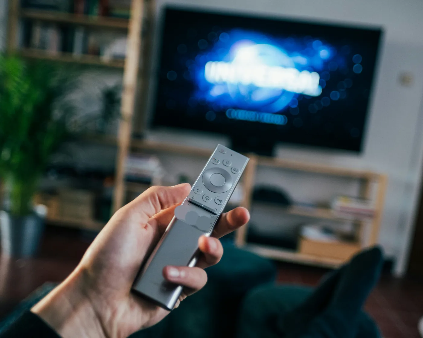 Main tenant une télécommande face à une Smart TV allumée dans un salon, illustration du blog IPTV France
